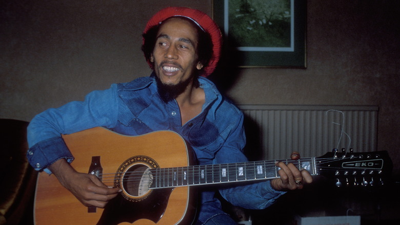Bob Marley playing guitar indoors smiling