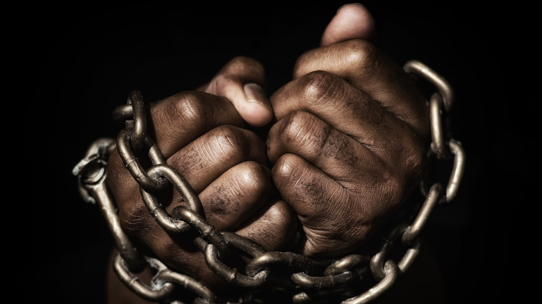 A man's hands bound in metal chains.