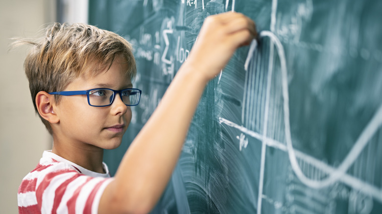 boy solving math equation on blackboard