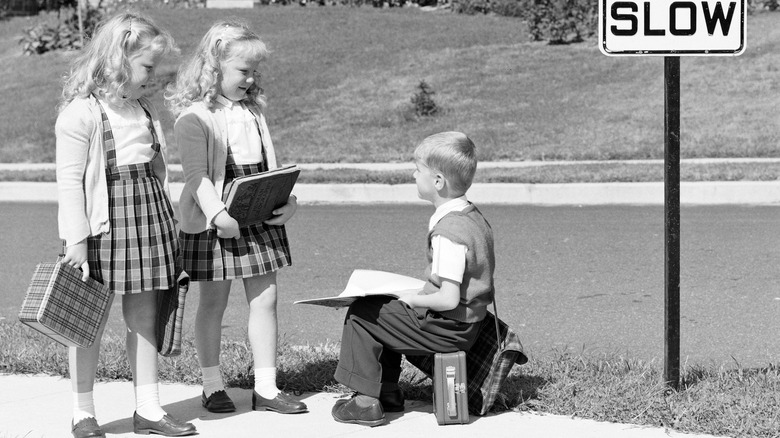 Two girls talking to boy while walking to school, 1953