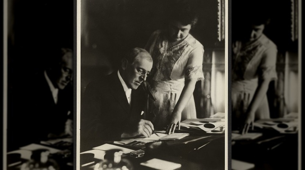 President Woodrow Wilson, seated at desk with his wife, Edith Bolling Galt, standing at his side