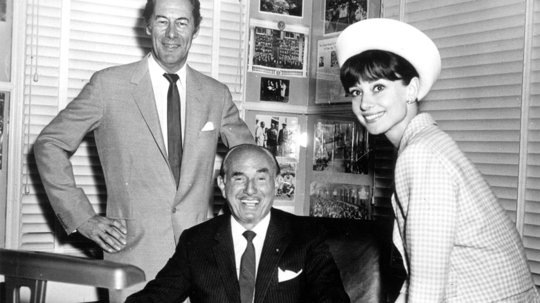 Rex Harrison and Audrey Hepburn standing over Jack Warner