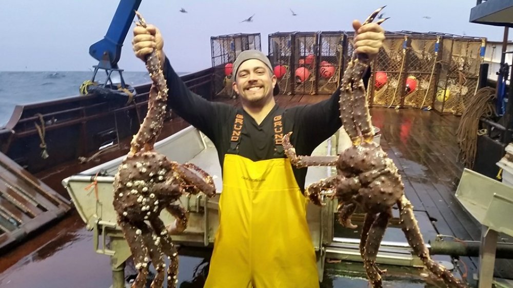 Mahlon Reyes smiling on boat holding up giant crabs