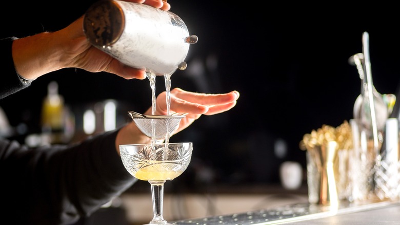 hands pouring cocktail into martini glass