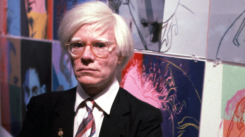 Andy Warhol poses by work