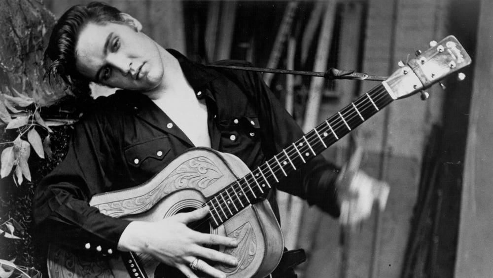 Elvis Presley poses for a portrait tilting his head to the side with guitar in hand