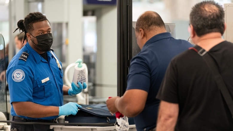 TSA officer in mask holding lotion inspecting bag
