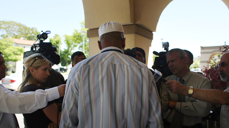 Imam speaking to reporters under archway