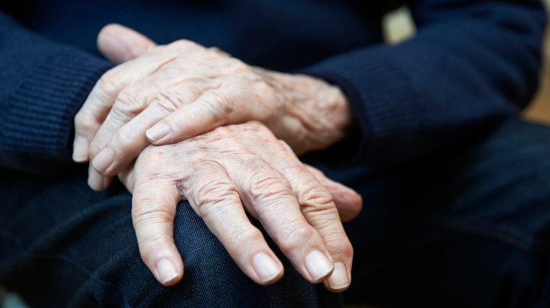 Elderly person gripping own hands