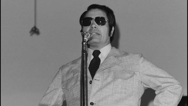 Jones in suit and sunglasses speaking in mic