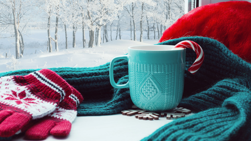 Winter scene with candy cane in mug alongside hat, scarf, mittens
